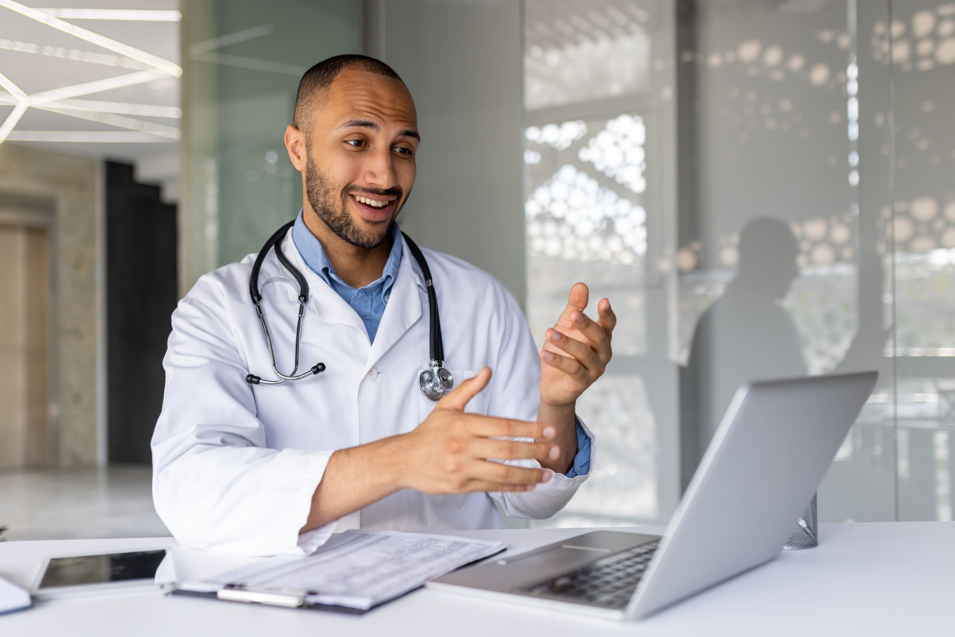 Confident doctor conducts telemedicine video call in modern office, using laptop for virtual medical consultation, showcasing healthcare technology digital communication